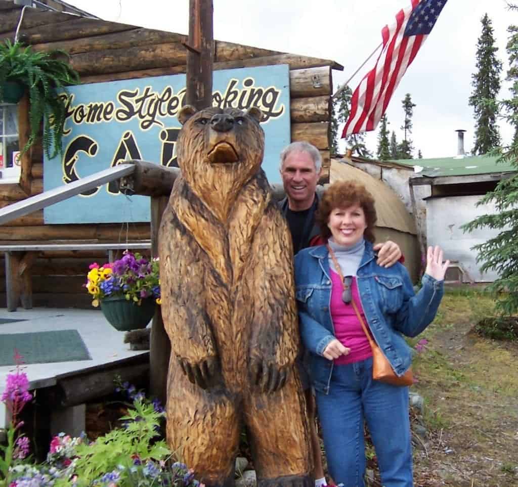 A couple posing in front of a carved bear during their Alaska vacation.