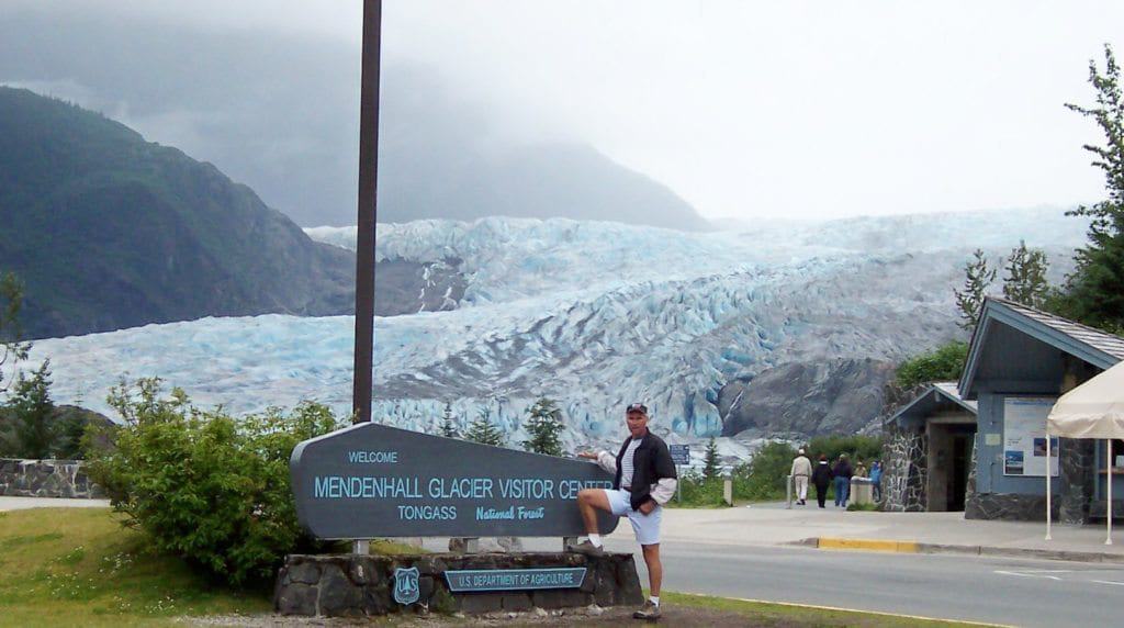 A man enjoying his Alaska vacation, standing in front of a glacier sign.