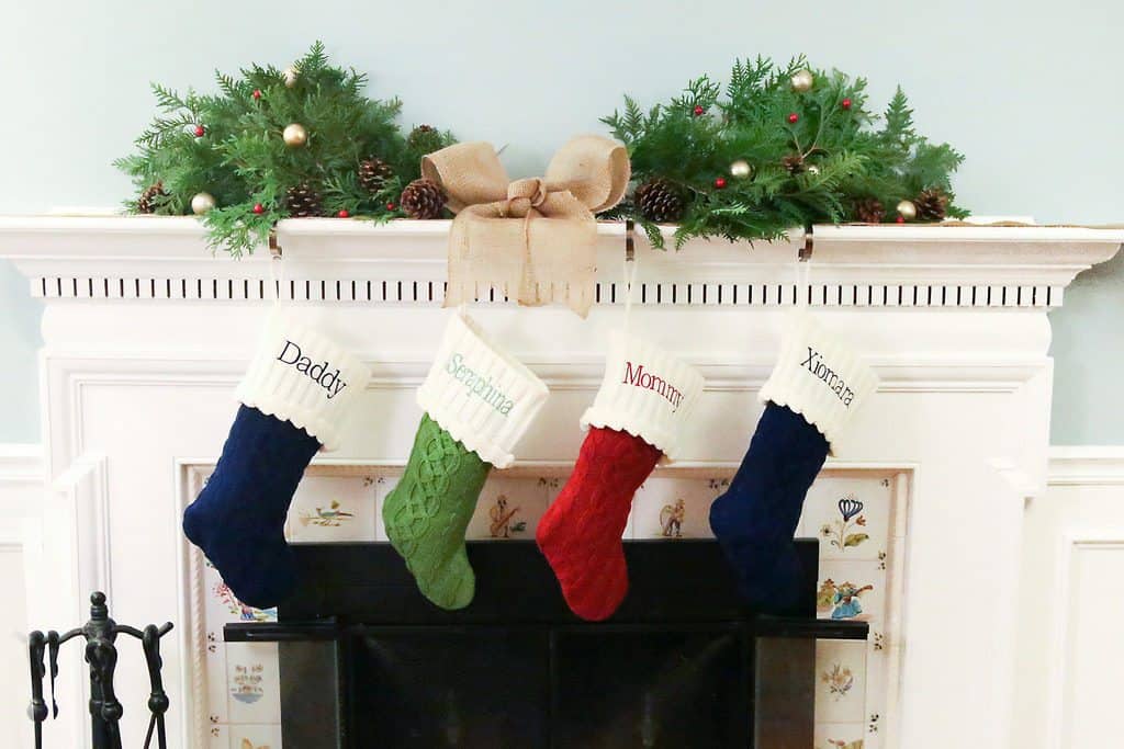 Personalized Christmas stockings displaying stocking stuffer ideas hang on a fireplace.