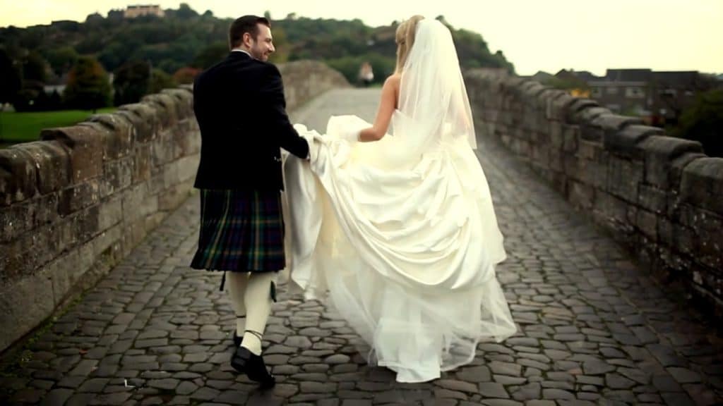 A European bride and groom strolling across a stone bridge.