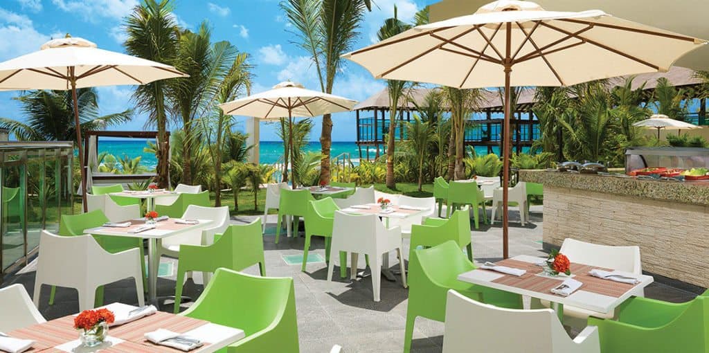A seaside restaurant with green chairs and umbrellas providing a serene atmosphere.