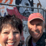 A couple enjoying European River Cruises while posing happily in front of a graffiti covered wall.