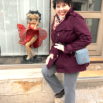 A woman standing in front of a store with a souvenir figurine.