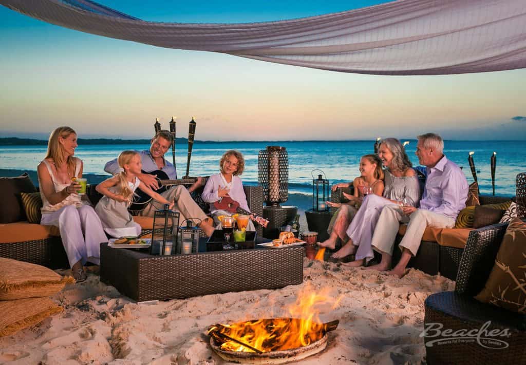 A family sitting around a fire pit on the beach at a family-friendly resort.