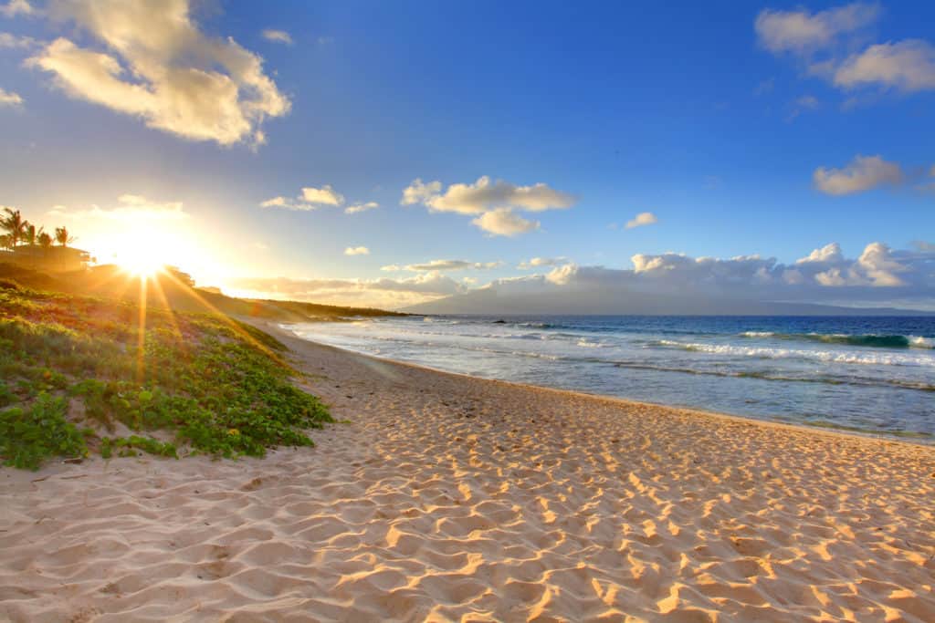 On a Maui vacation, the sun is shining over a sandy beach and ocean.