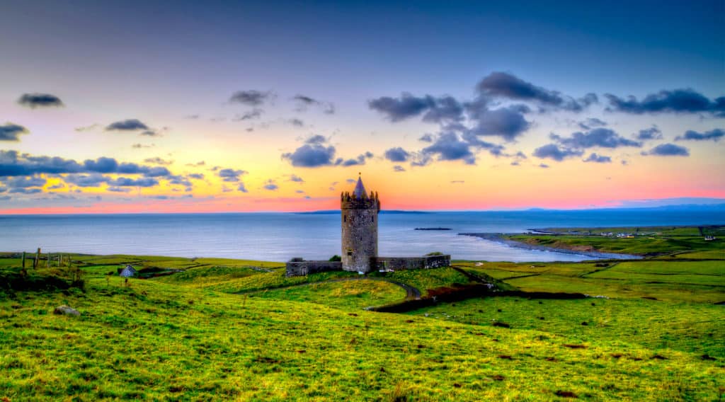 A tower in Ireland sits on top of a green hill overlooking the ocean.