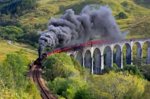 A steam train resembling the iconic Hogwarts Express soaring across a viaduct in Scotland.