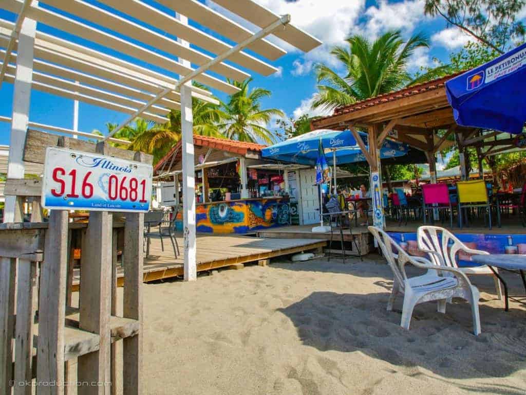 An adult-friendly beach bar with tables and chairs on the sand, perfect for Caribbean travel.