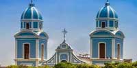 White church with two blue domes under a clear Caribbean sky.