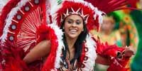 A woman in a vibrant red carnival costume with elaborate feathered headdress smiling during a Caribbean adventure.