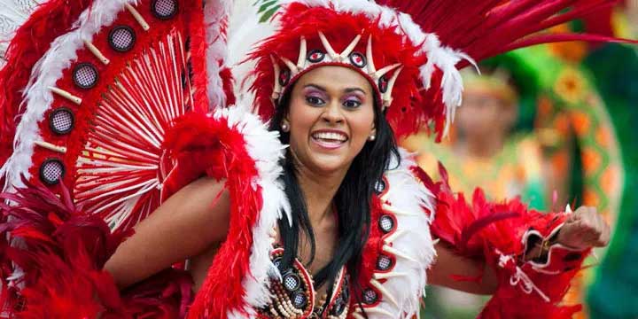 Woman in vibrant red carnival costume with large feathered headdress dancing at a Caribbean festival.