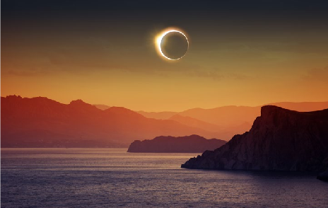 A solar eclipse over a coastal landscape with mountains in the background. The sky is lit with warm colors from the setting sun, reminiscent of the vibrant hues of the Northern Lights.