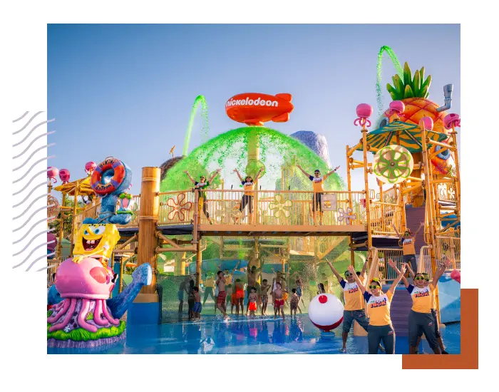 People are enjoying a vibrant and inclusive water park featuring Nickelodeon-themed decorations with characters and a play structure under sprays of water.