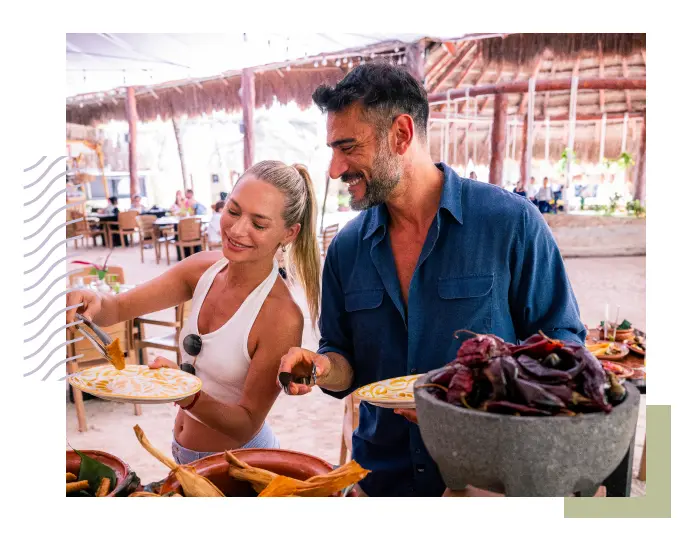 A woman and a man are serving food onto plates from a buffet table in an open-air dining area. The setting, adorned with thatched roofing and wooden furniture, offers a more inclusive atmosphere for everyone to enjoy.