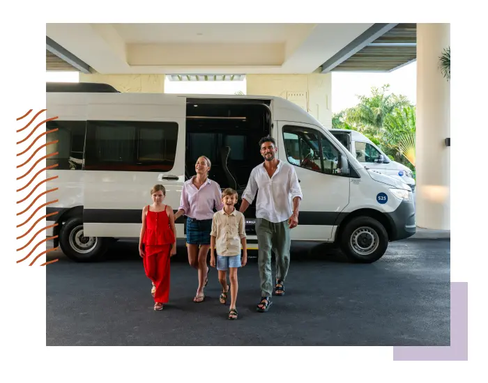 A family of four, two adults and two children, walk away from a white passenger van parked under a canopy, embodying the spirit of MORE INCLUSIVE™ living.