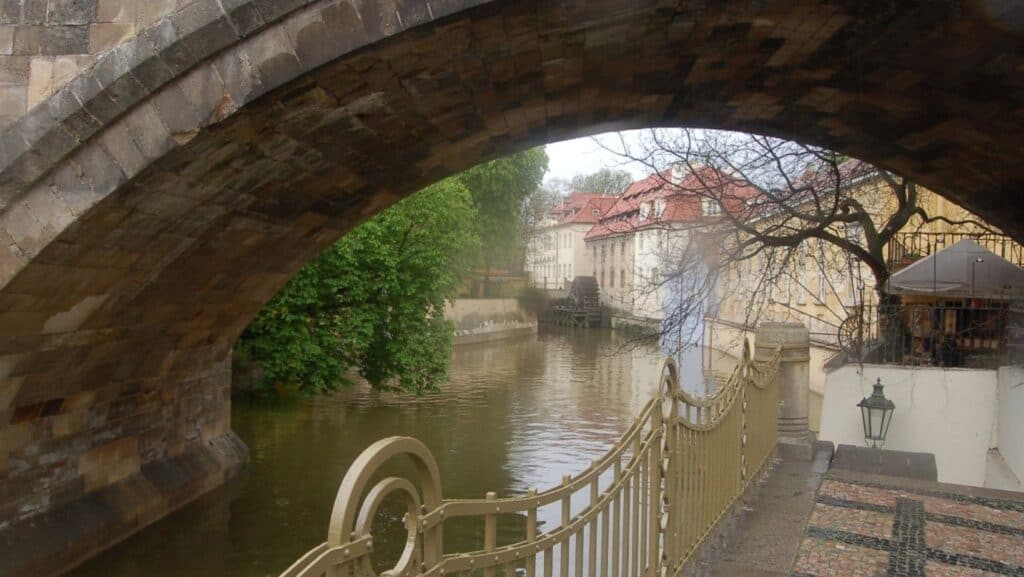 The stone bridge gracefully arches over a canal, perfect for romantic getaways, lined with trees and historic buildings. A wrought iron fence traces the path, while a lamppost casts a soft glow on the right.