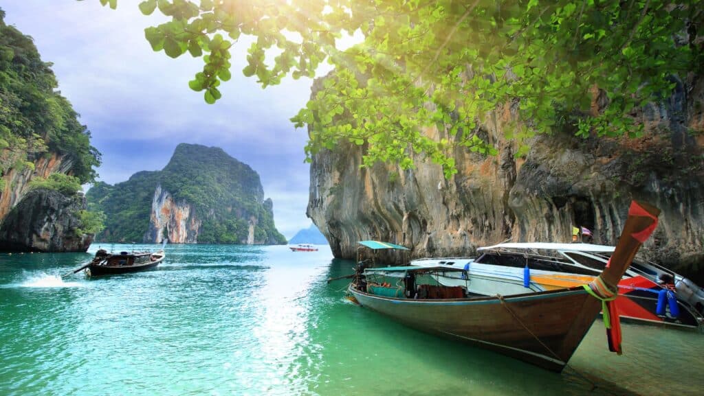 Boats float in a clear turquoise bay, ideal for couples vacations, surrounded by tall limestone cliffs and lush greenery under a bright sky.