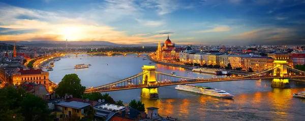 A panoramic view of Budapest at sunset, featuring the Chain Bridge and Parliament building along the Danube River, glistening as city lights illuminate. Perfect for those embarking on a memorable Danube River Cruise!.