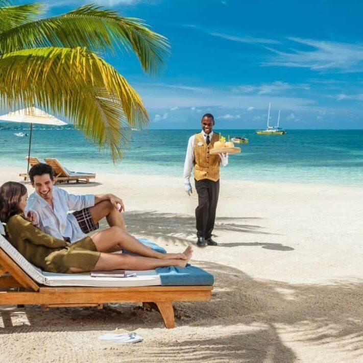 Two people sitting on lounge chairs at a Sandals Resorts beach.