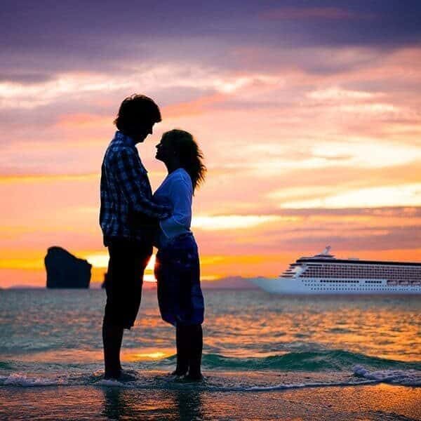 A couple standing on the beach with a Gourmet All Inclusive cruise ship in the background.