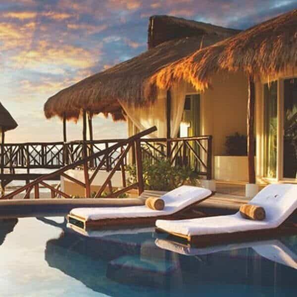 Two lounge chairs next to a pool with thatched roofs, offering a Gourmet All Inclusive experience.