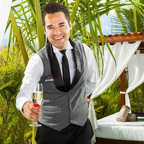 A waiter at Karisma Resorts holding a glass of champagne in front of a palm tree.